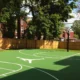 Backyard basketball court with green FlexCourt modular tiles, white game lines, and hoop in a fenced residential yard.